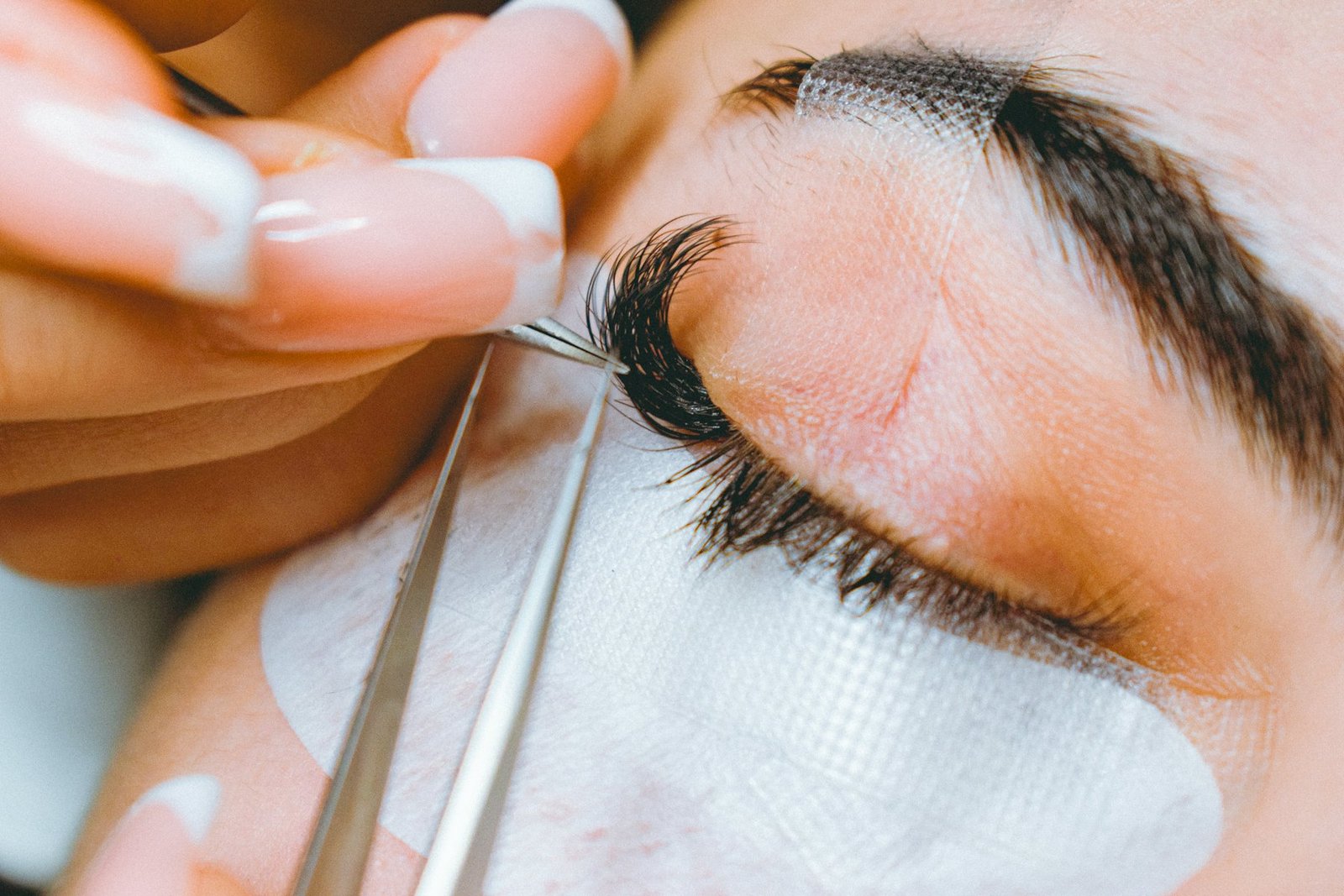 Profissional aplicando extensão de cílios fio a fio em uma cliente